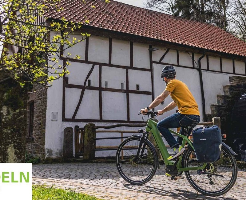 Mann auf einem Fahrrad vor einem Wasserrad